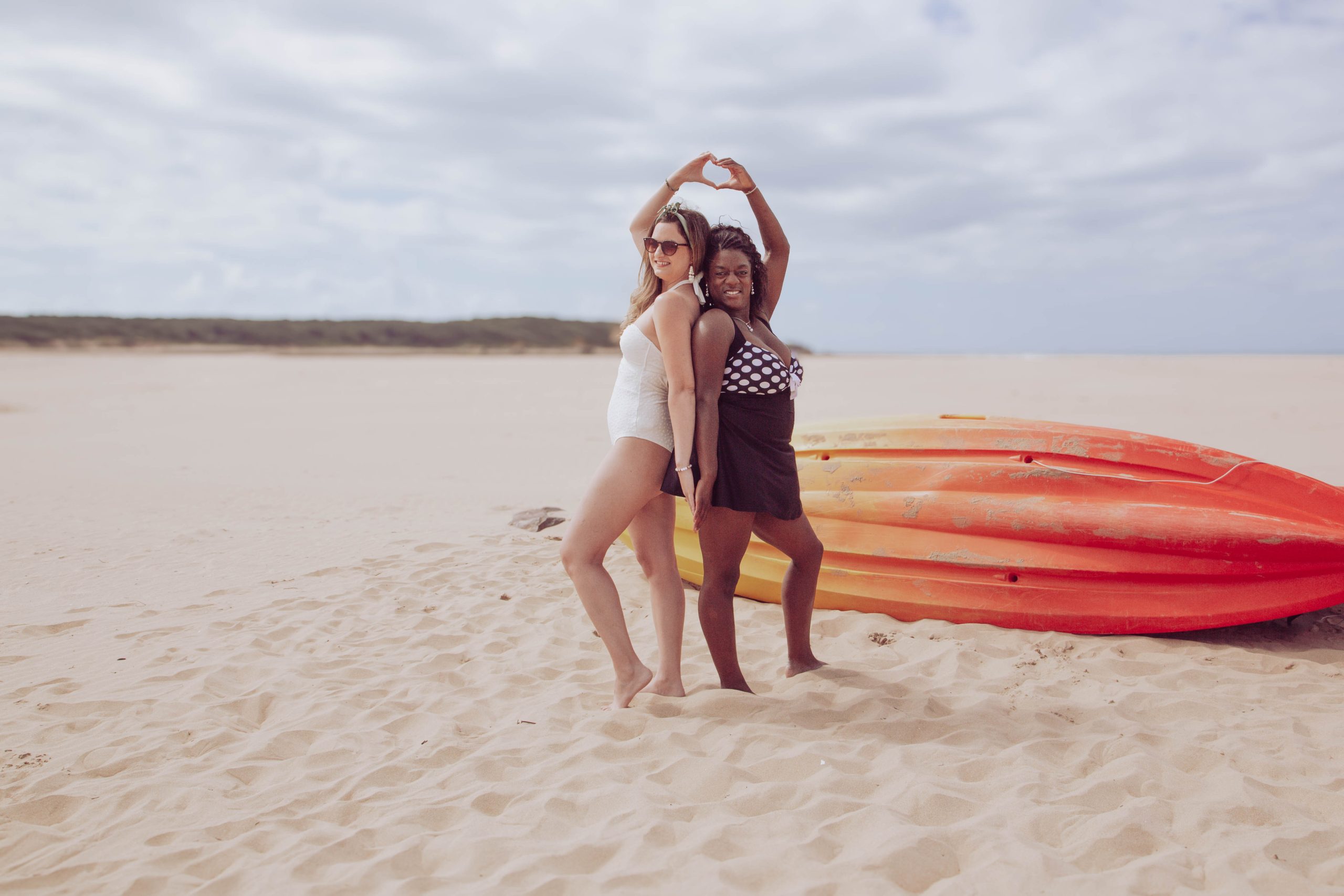 Entretien-bilan Deux femmes debout sur une plage de sable, posant ensemble de façon amicale.